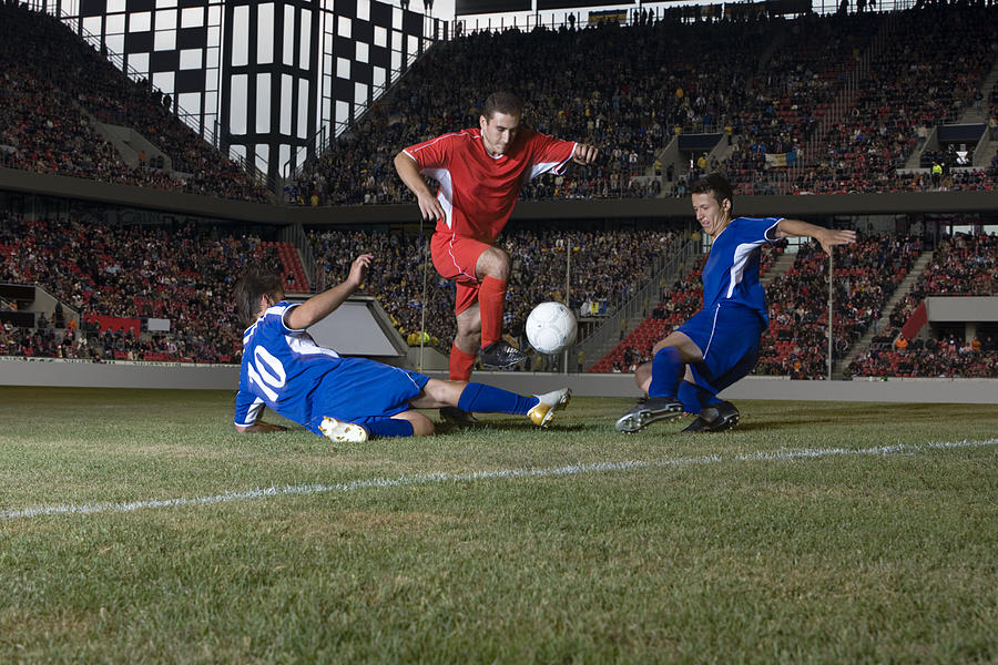 Opposite players tackling footballer Photograph by Image Source