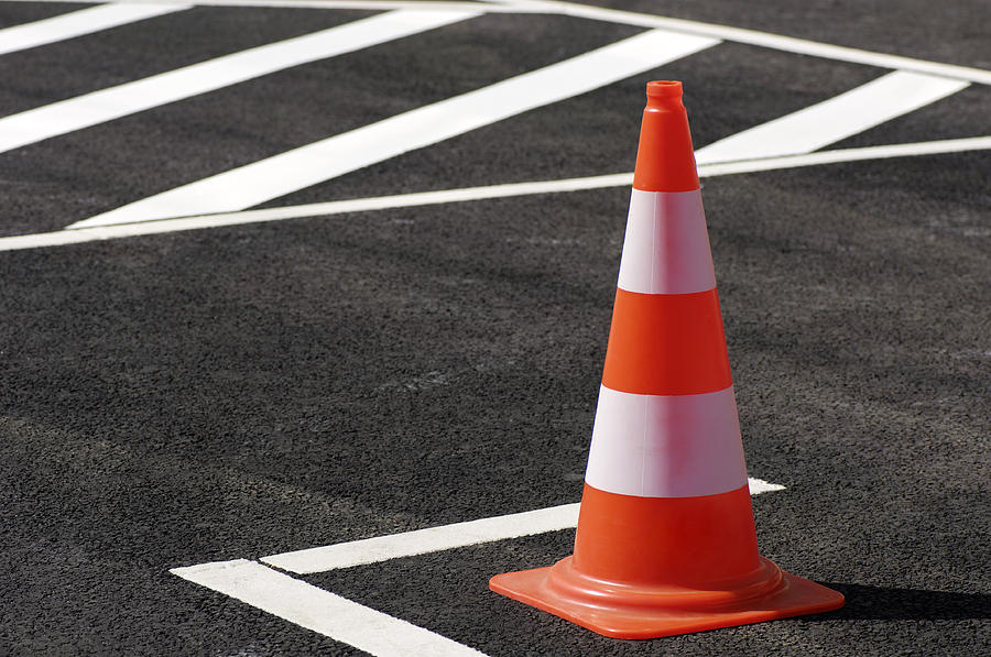 Orange traffic cone sitting on the black top pavement Photograph by Acilo