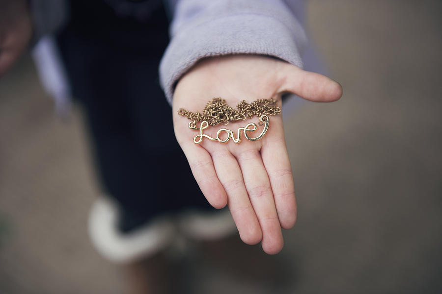 Overhead view of hand holding locket with love text on street Photograph by Cavan Images