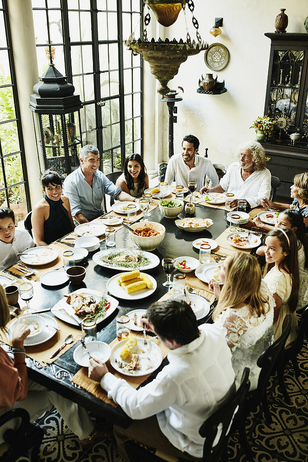 Overhead view of multigenerational family gathered at dining room table for celebration meal Photograph by Thomas Barwick