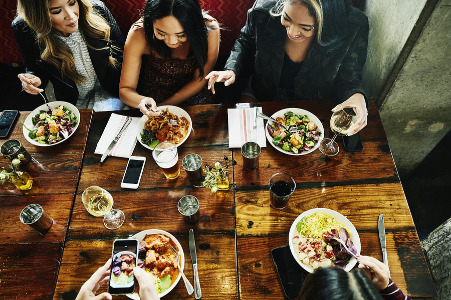 Overhead view of smiling female friends sharing lunch in restaurant Photograph by Thomas Barwick