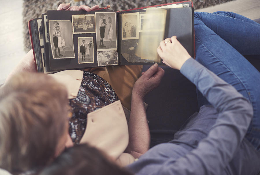 Overhead view of young woman on sofa with grandmother looking at photo album Photograph by Gpointstudio