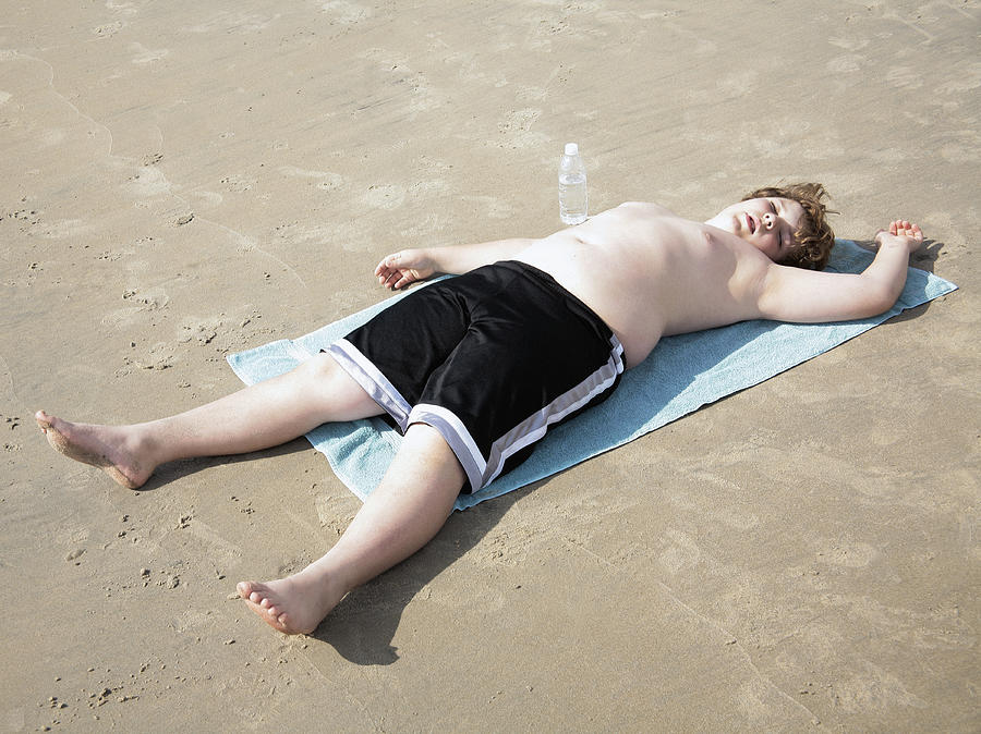 Overweight boy lying on towel on beach Photograph by Steven Puetzer