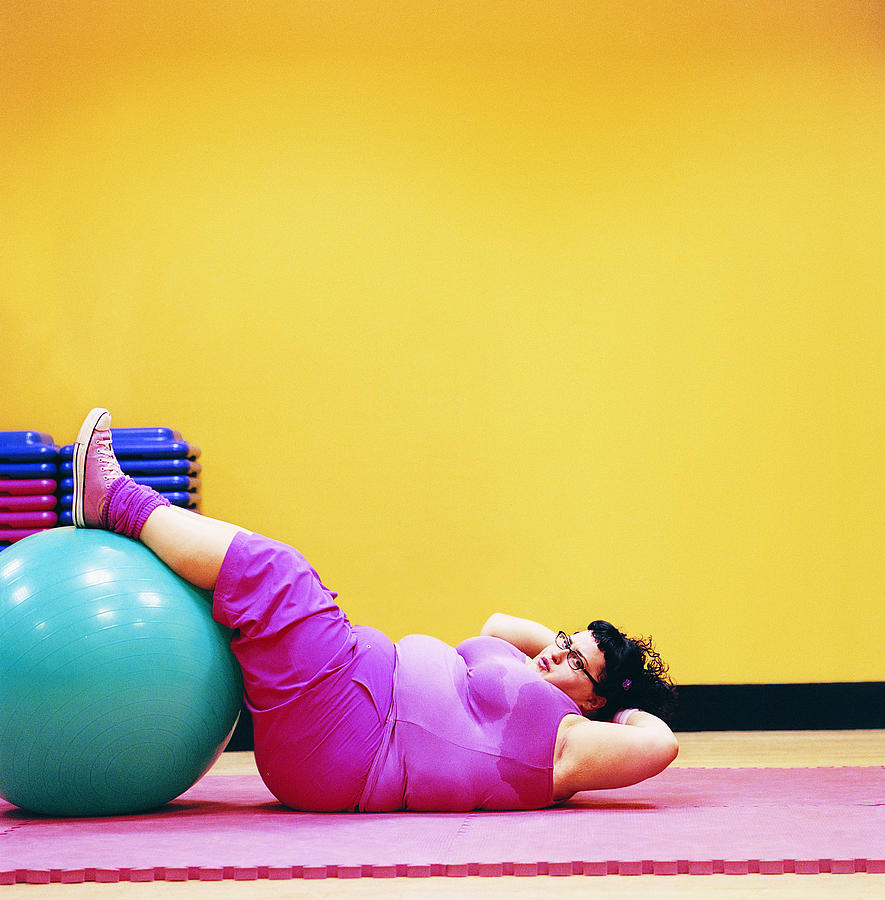 Overweight Woman Doing Sit Ups in a Gym With Her Feet Up on an Exercise Ball Photograph by Digital Vision.