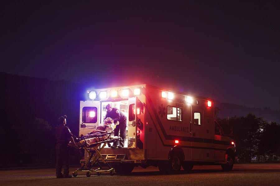 Paramedics carrying patient in ambulance at night Photograph by Cavan Images