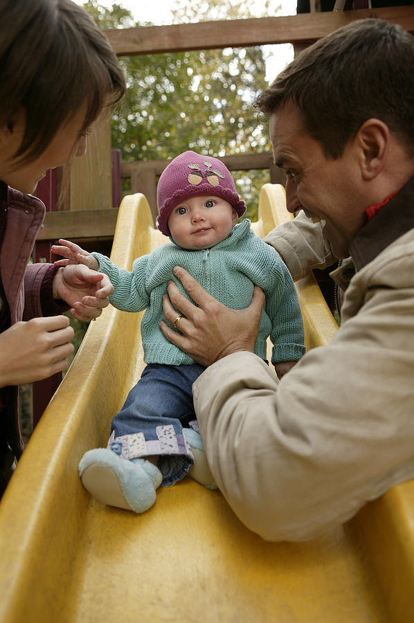 Parents with baby playing on slide Photograph by Comstock Images