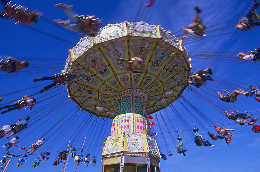 People sitting on carousel swings ride, low angle view Photograph by Stuart Gregory