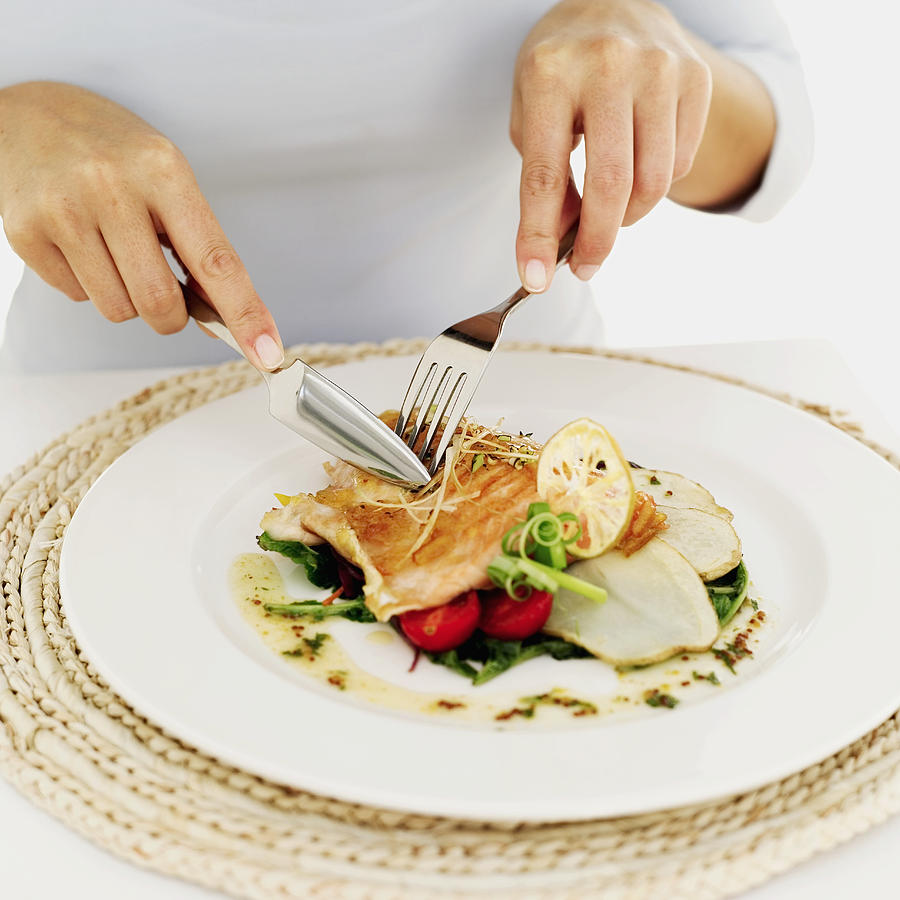 Person Using A Fork And Knife On A Plate Of Grilled Salmon Photograph by Stockbyte