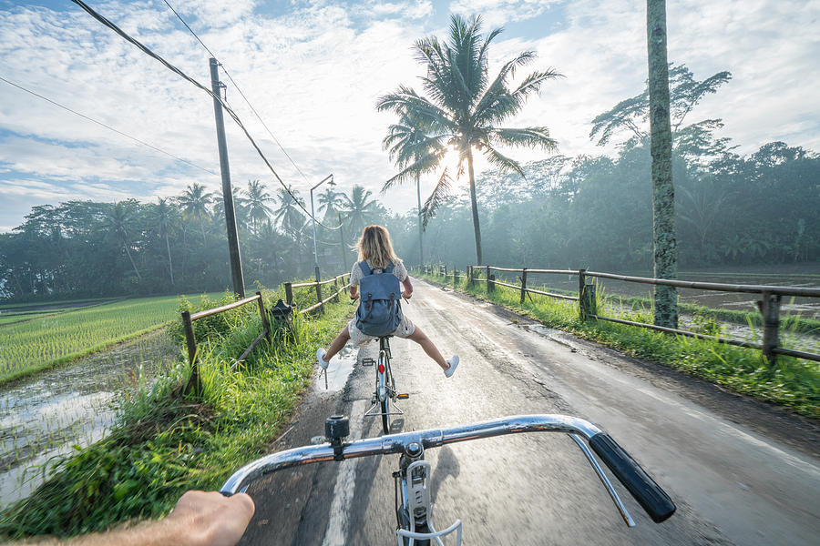 Personal perspective- couple cycling near rice fields at sunrise, Indonesia Photograph by Swissmediavision