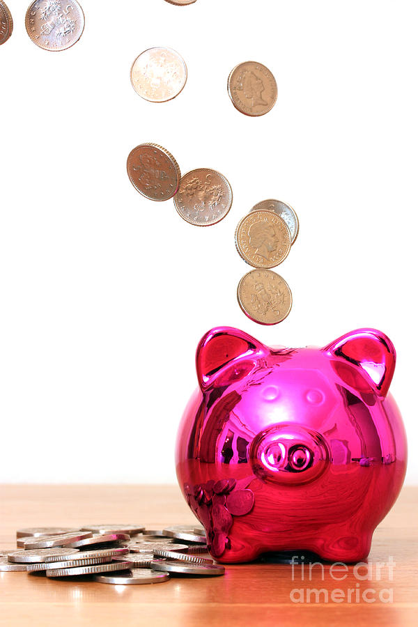 Piggy bank saving with money pouring into it Photograph by Simon Bratt