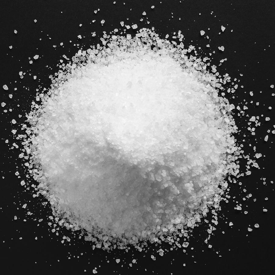 Pile of coarse sea salt grains on a black background. Photograph by Mint Images - Paul Edmondson