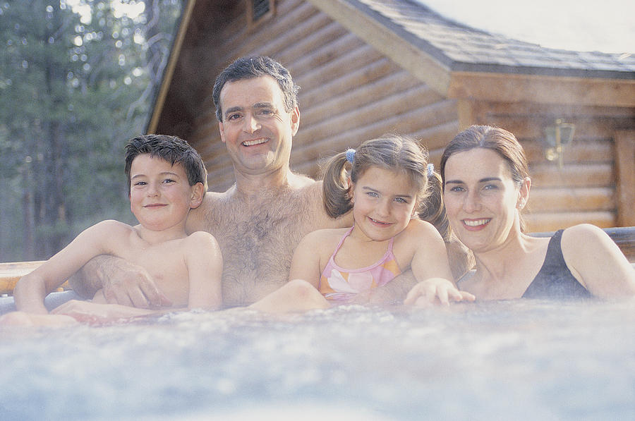 Portrait of a Family of Four Relaxing in a Hot Tub in Front of a Snow Covered Chalet Photograph by Digital Vision.