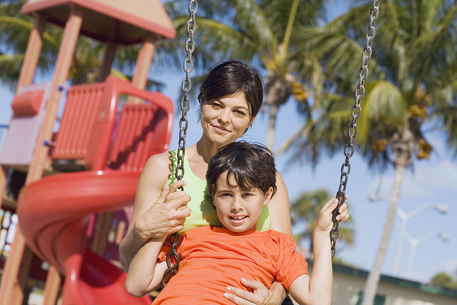 Portrait of a mid adult woman swinging on a swing with her son and smiling Photograph by Glowimages