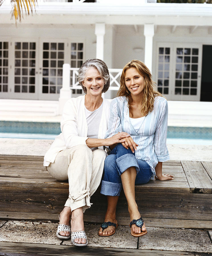 Portrait of a Senior Woman and Her Mature Daughter Sitting on Poolside Decking Photograph by Digital Vision.