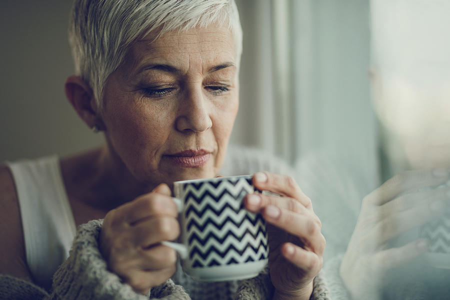 Portrait of a senior woman with coffee cup by the window. Photograph by Skynesher