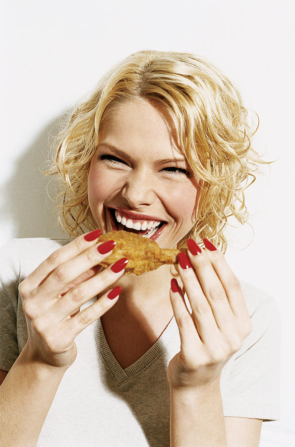 Portrait of a Smiling, Young Woman Eating a Deep Fried Chicken Drumstick Photograph by Digital Vision.