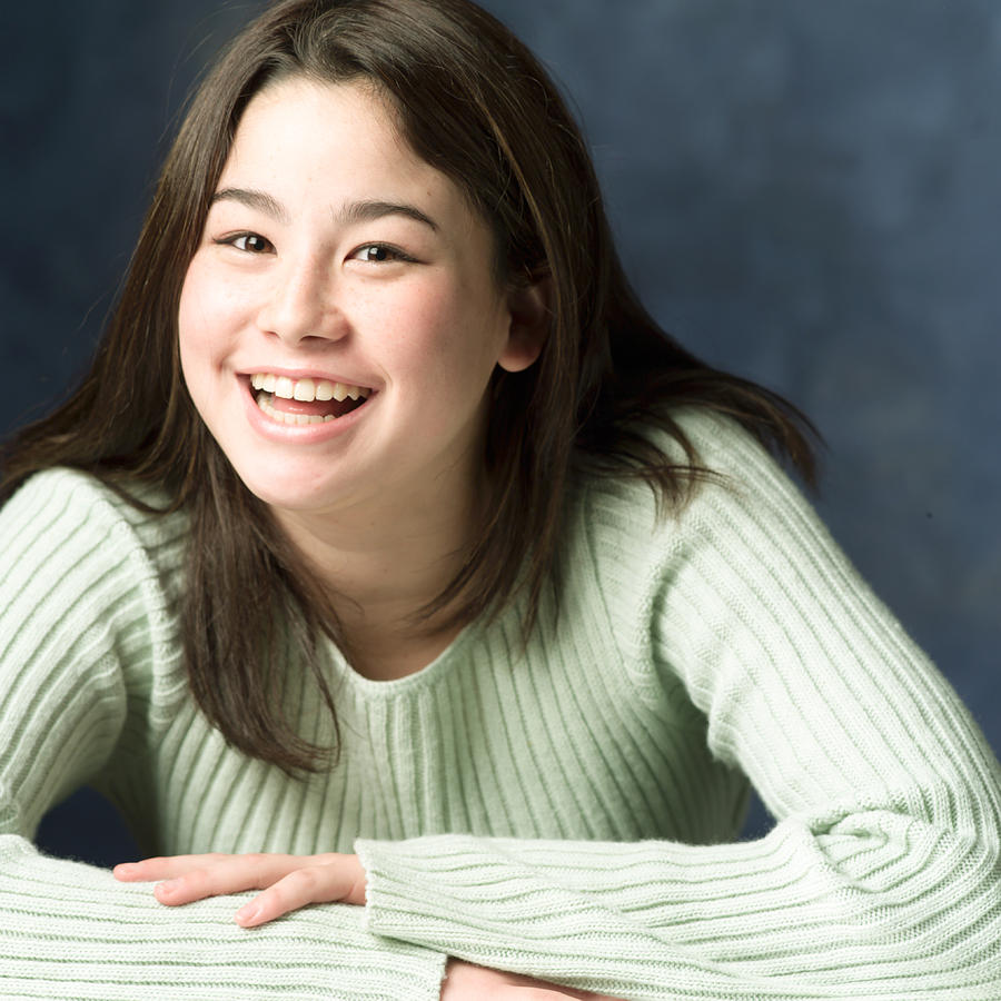 Portrait Of A Teenage Asian Girl In A Green Sweater As She Crosses Her Arms Leands Forward And Smiles Photograph by Photodisc