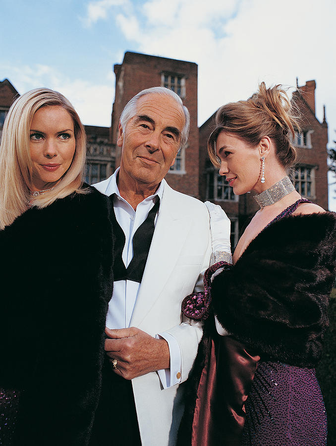 Portrait of a Wealthy Senior Man Standing Between Two Young Women Photograph by Digital Vision.