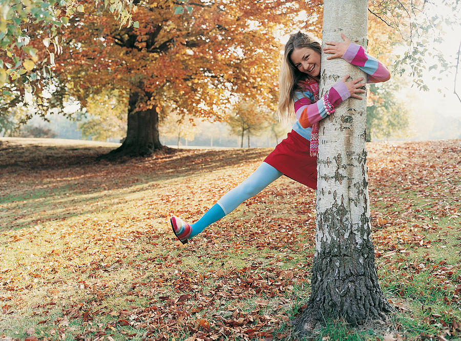Portrait of a Young Woman on one Leg Laughing With Her Arms Around a Tree Photograph by Digital Vision.