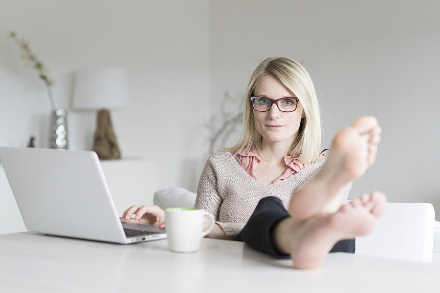 Portrait of blond woman at home sitting at table with feet up Photograph by Westend61