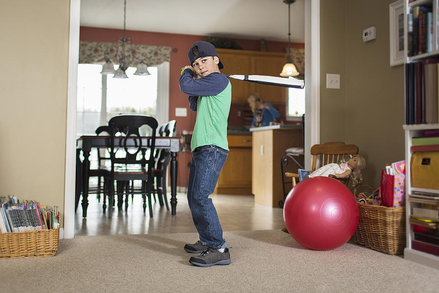 Portrait of boy practicing baseball in sitting room Photograph by Steve Prezant