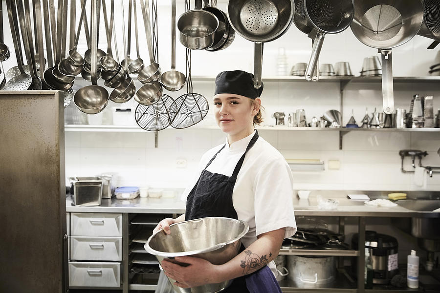 Portrait of confident female chef holding container in commercial kitchen Photograph by Maskot