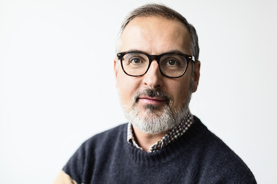 Portrait of confident mature man wearing eyeglasses against white background Photograph by Maskot