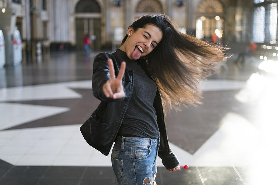 Portrait of exuberant young woman with lollipop in station concourse Photograph by Westend61