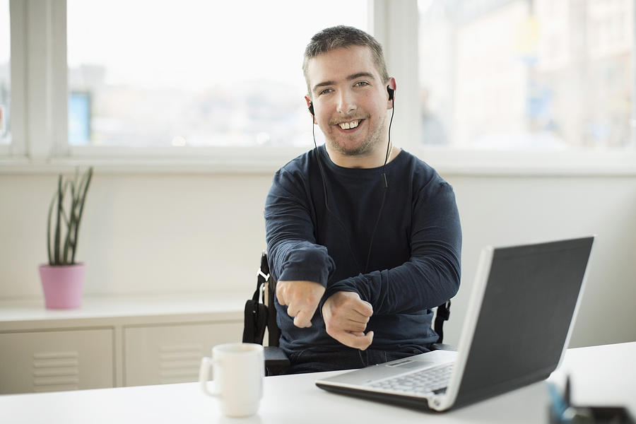 Portrait of happy disabled businessman with laptop at desk in office Photograph by Maskot