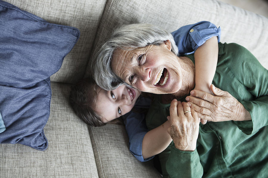 Portrait of laughing grandmother and her granddaughter on the couch Photograph by Westend61