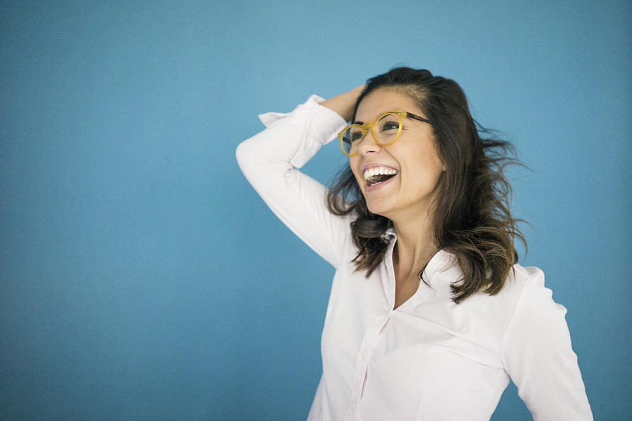 Portrait of laughing woman wearing glasses in front of blue background Photograph by Westend61