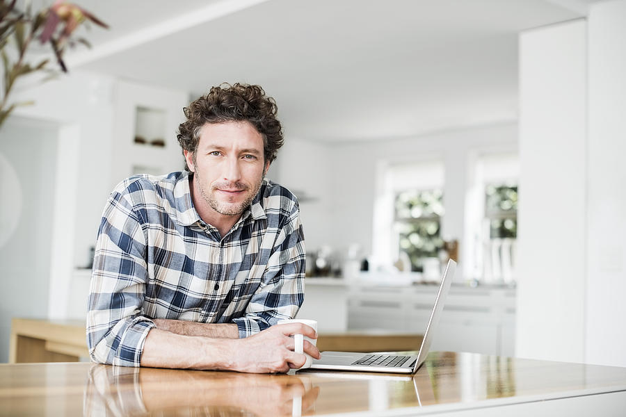 Portrait of man having coffee while using laptop Photograph by Portra