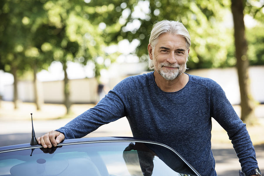 Portrait of mature grey haired Man leaning on car Photograph by Robin Skjoldborg