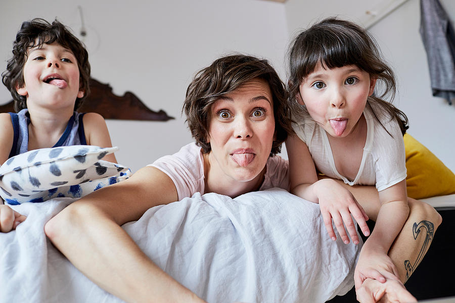 Portrait of mother, son and daughter, lying on bed, poking tongue out Photograph by Emely