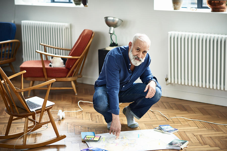 Portrait of senior man crouching on floor with map Photograph by 10000 Hours