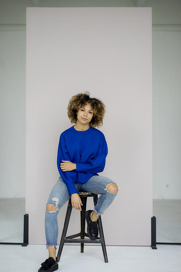 Portrait of serious woman wearing blue pullover sitting on stool Photograph by Westend61