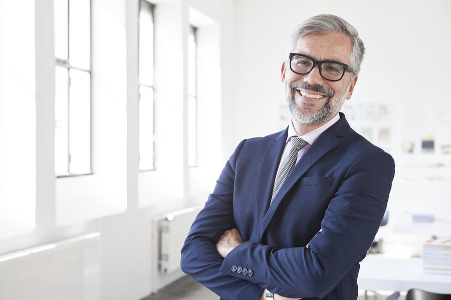 Portrait of smiling businessman with crossed arms in an office Photograph by Westend61