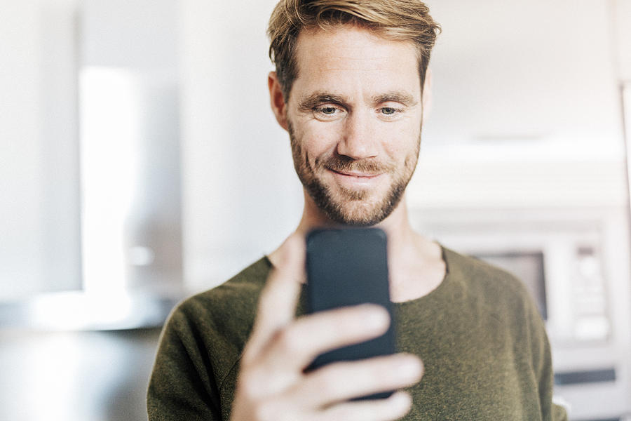 Portrait of smiling man looking at cell phone Photograph by Westend61