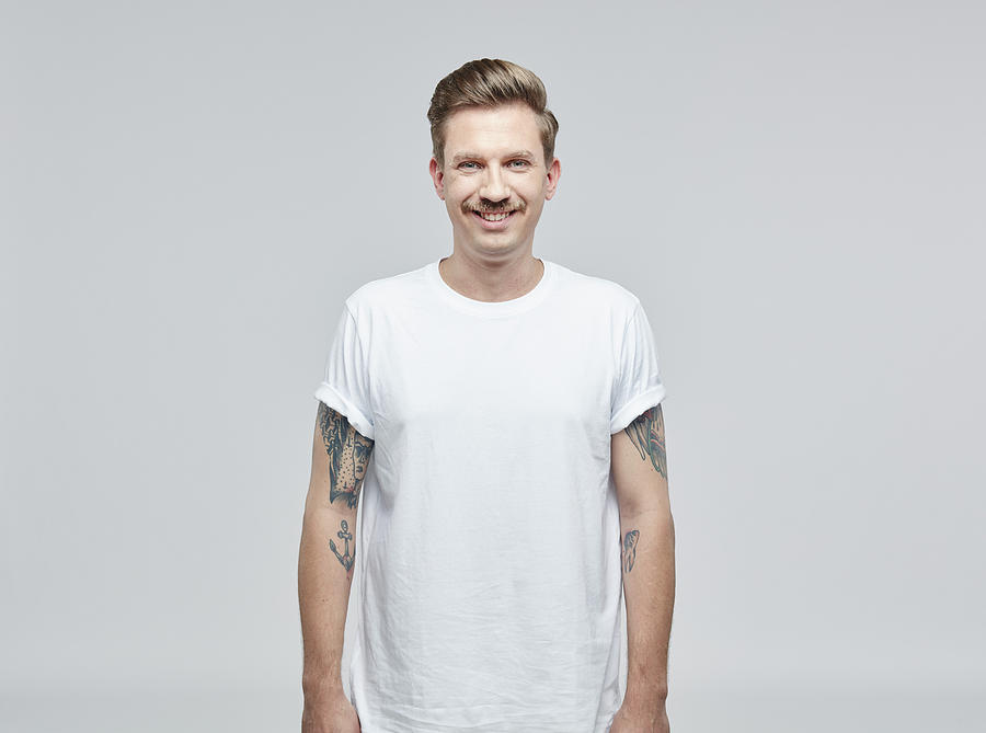 Portrait of smiling man with tatoos on his arms wearing white t- shirt in front of grey background Photograph by Westend61