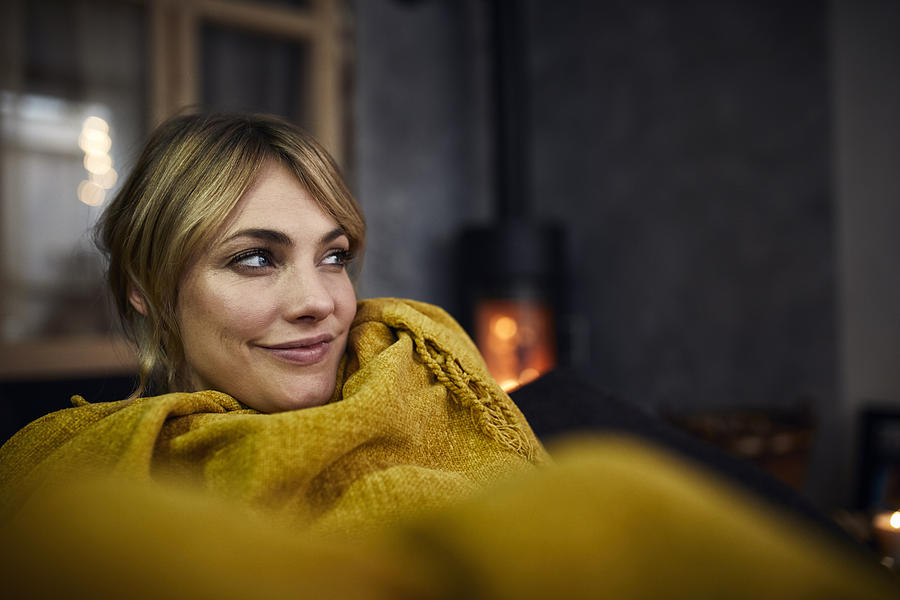 Portrait of smiling woman relaxing on couch at home in the evening Photograph by Westend61