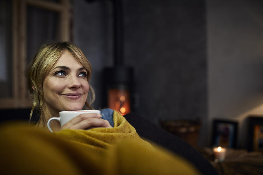 Portrait of smiling woman with cup of coffee relaxing on couch at home in the evening Photograph by Westend61
