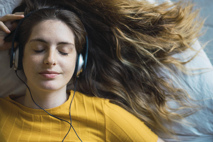 Portrait of smiling young woman lying on bed listening music with headphones Photograph by Westend61