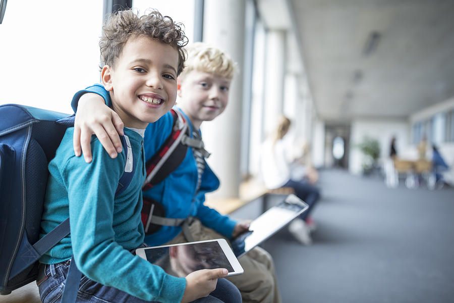 Portrait of two smiling schoolgboys with tablet embracing Photograph by Westend61