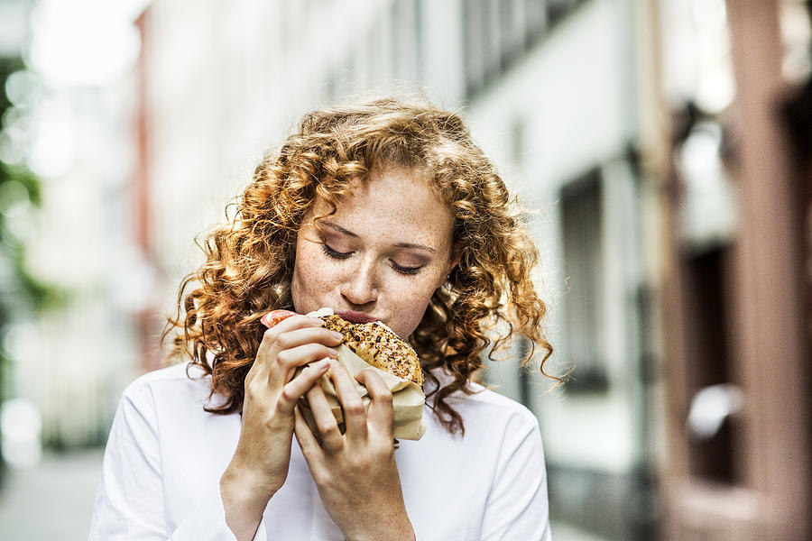Portrait of young woman eating bagel outdoors Photograph by Westend61