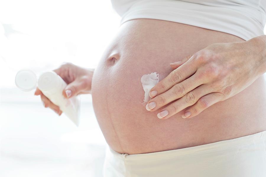 Pregnant Woman Applying Moisturiser To Her Tummy Photograph By Ian