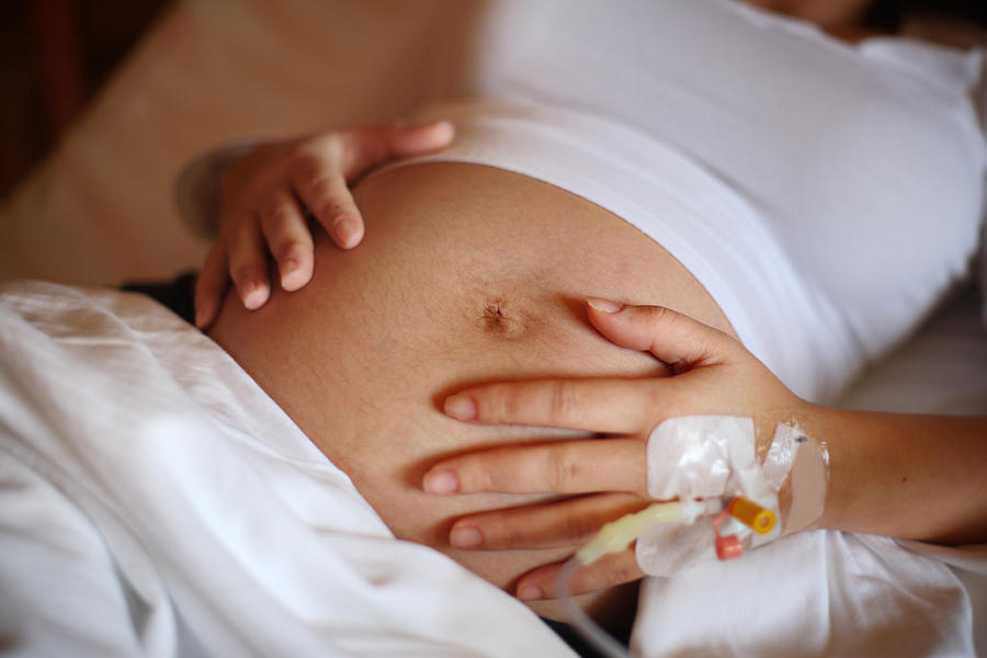 Pregnant woman holding her belly, attached to medical tubes Photograph by Ciseren