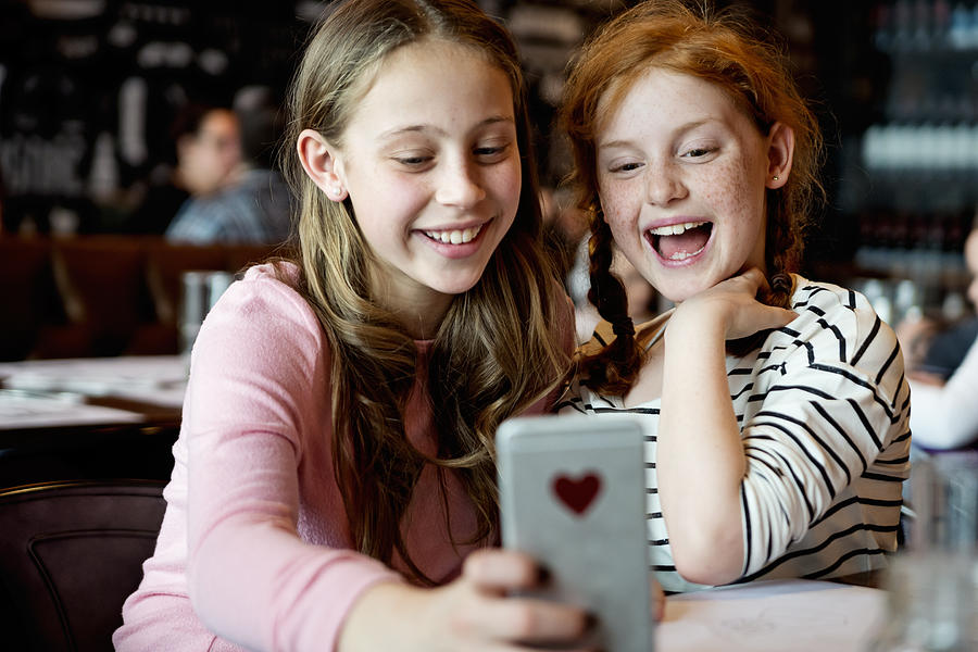 Preteens girls doing selfies at a restaurant table. Photograph by Martinedoucet