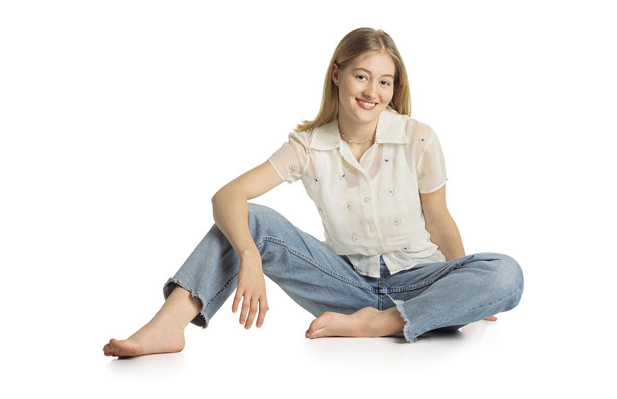 Pretty Young Teenage Girl With Long Blonde Straight Hair Wearing A Cream Short-sleeved Shirt And Blue Jeans Sits On The Ground And Smiles At The Camera Photograph by Photodisc