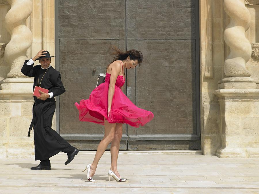 Priest passing woman whose skirt is blowing up in the wind, Alicante, Spain, Photograph by Dev Carr