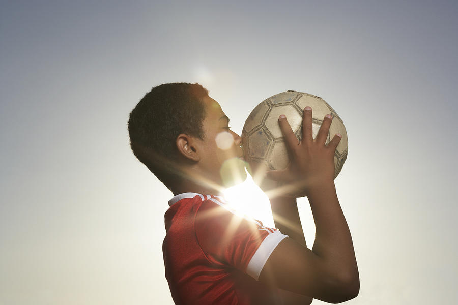 Profile of boy (12-13) kissing football, lens flare Photograph by Roger Weber